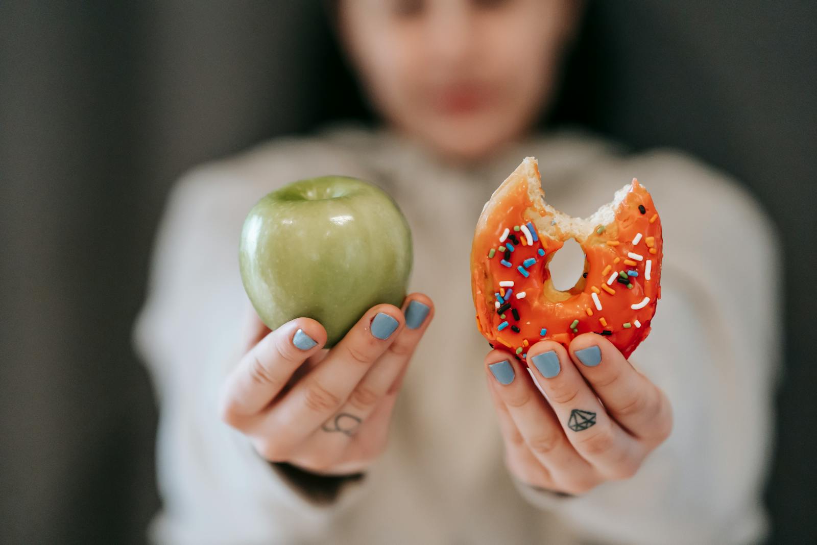 Dieta 5 posiłków dziennie - zasady, korzyści i przykłady меню A close-up of a person holding an apple and a donut, symbolizing the choice between healthy eating and indulgence.